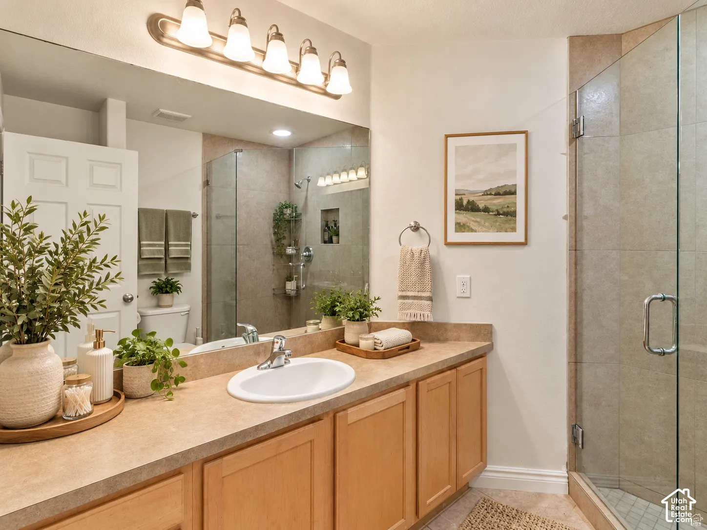 Bathroom vanity featuring wood cabinetry, a solid surface countertop with an integrated basin, a full-width mirror, five-light fixture, and a glass-enclosed shower with tiled surround