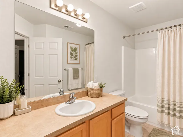 Bathroom featuring a vanity with wood-finish cabinetry, an integrated sink, a large wall-mounted mirror, and a tub-shower combination with a surround
