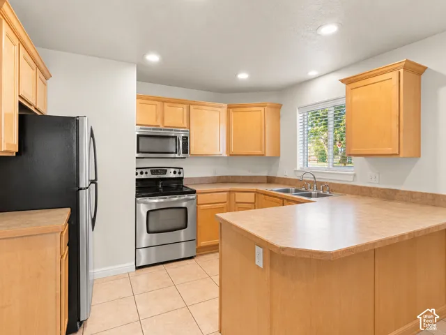 Kitchen featuring natural wood cabinetry, laminate countertops, stainless steel appliances, tile flooring, and recessed lighting