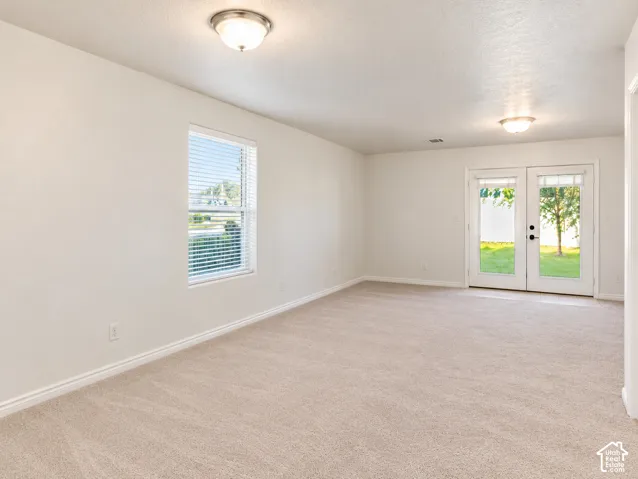 Neutral wall-to-wall carpeting, dual flush-mount ceiling light fixtures, single-hung window, and glass-paned double doors