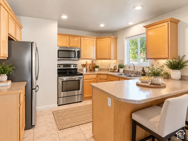 Kitchen featuring natural-finish cabinetry, stainless steel appliances, solid-surface countertops, recessed lighting, and tile flooring