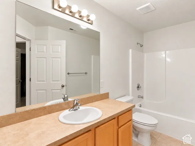 Bathroom featuring a vanity with wood-finish cabinetry, integrated countertop with a white oval basin, a full-width mirror, a multi-bulb light fixture, and a white tub-shower combination