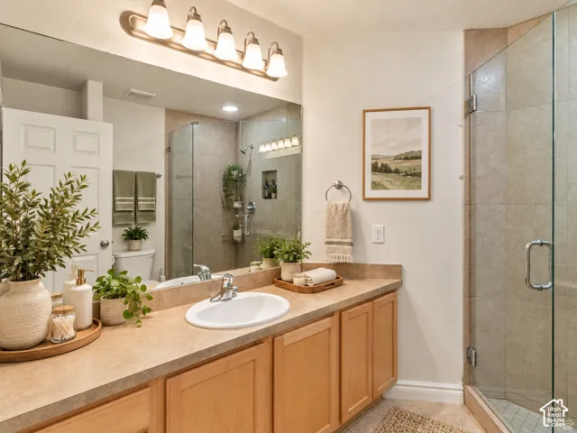 Bathroom vanity featuring wood cabinetry, a solid surface countertop with an integrated basin, a full-width mirror, five-light fixture, and a glass-enclosed shower with tiled surround
