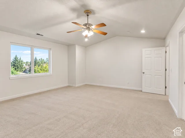 Vaulted ceiling room featuring neutral carpeting, a dual-tone metal ceiling fan with integrated lighting, and a six-panel door