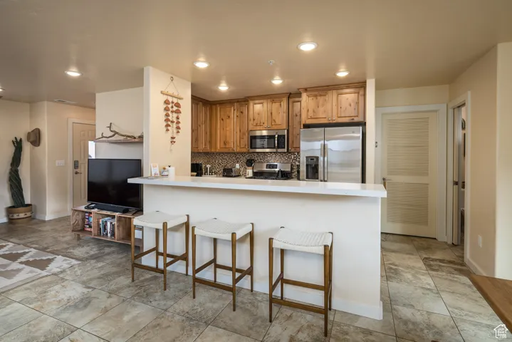 Kitchen with a peninsula, decorative backsplash, stainless steel appliances, a kitchen breakfast bar, and light countertops