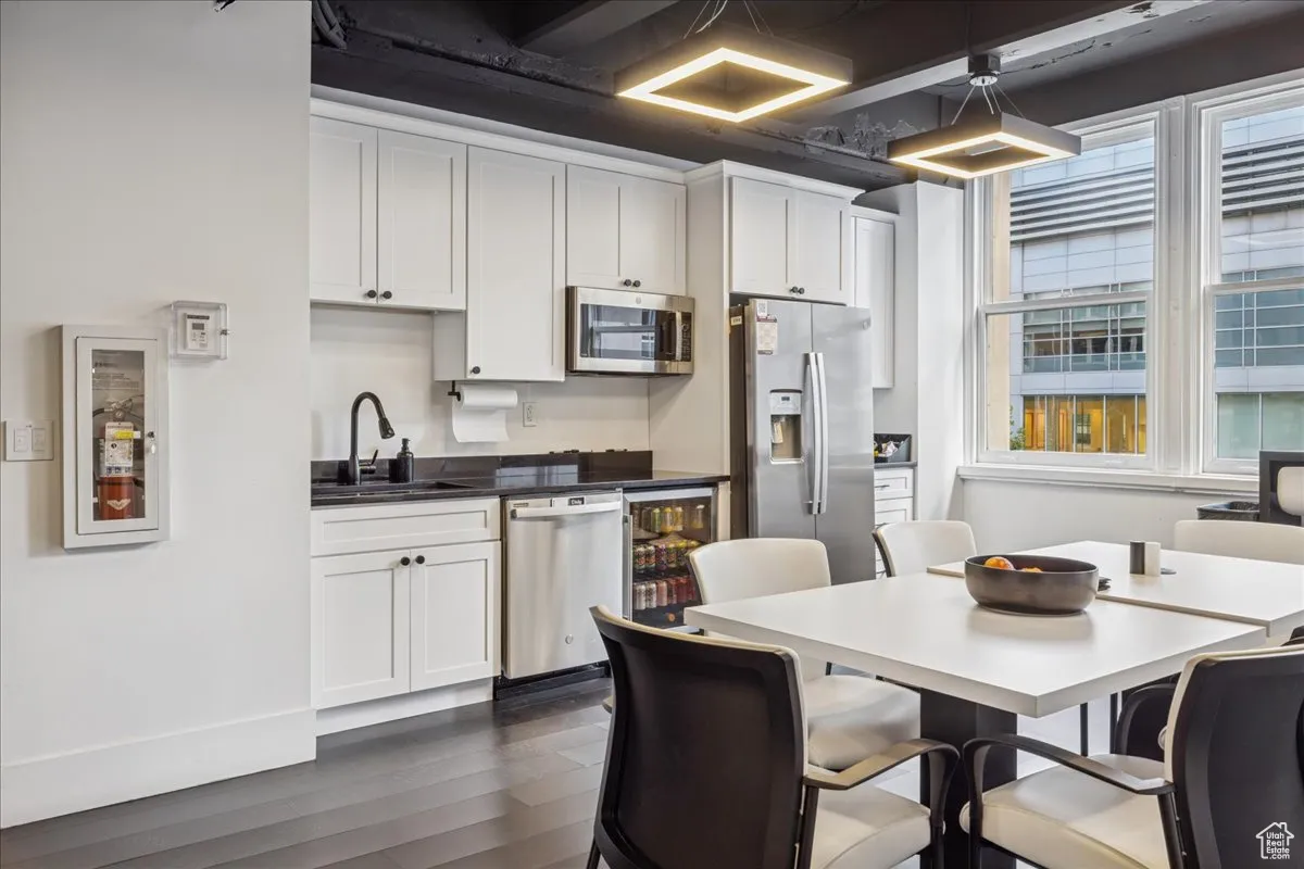 Kitchen with white cabinetry, stainless steel appliances, dark wood-style floors, dark countertops, and beverage cooler