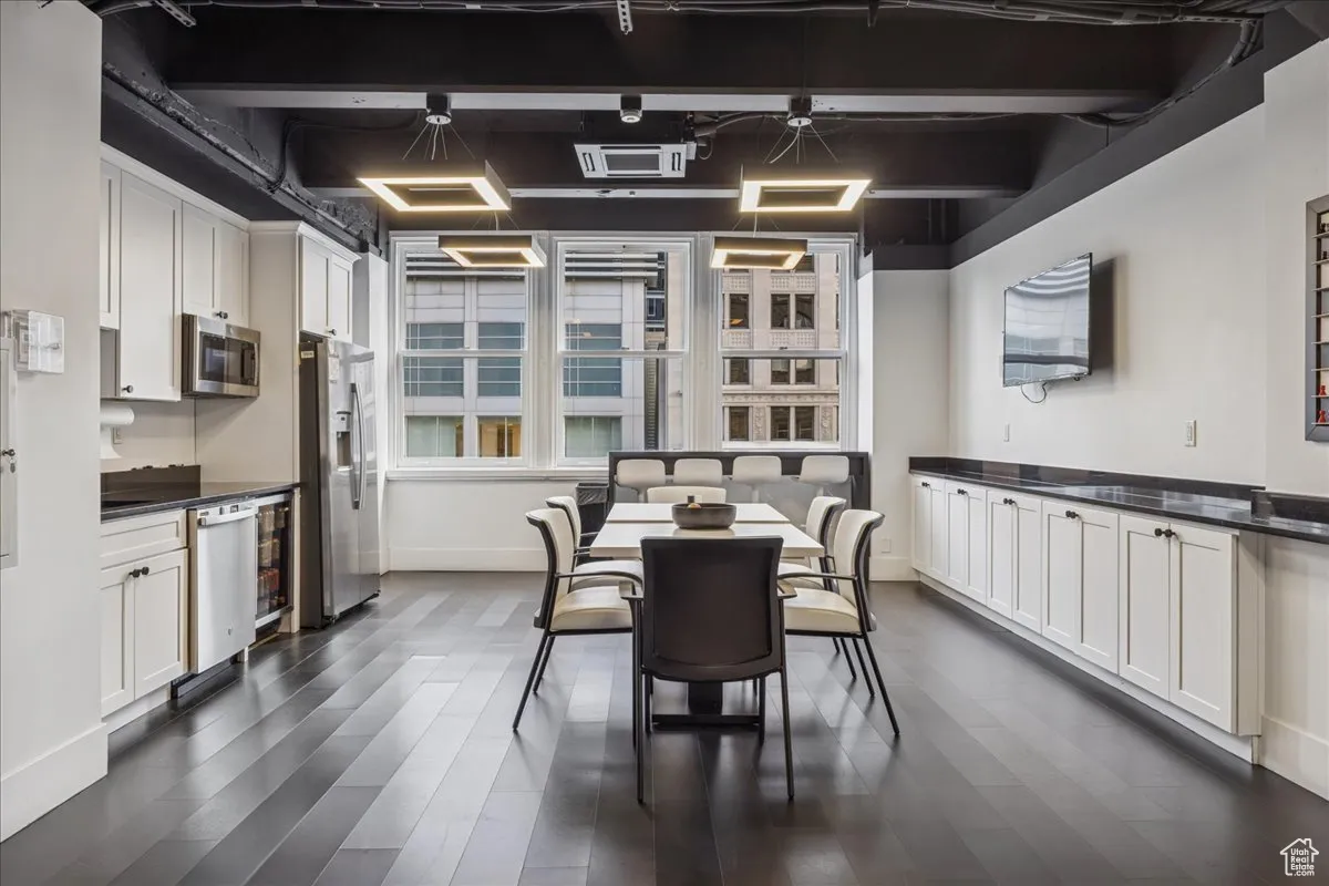 Kitchen featuring white cabinetry, dark wood-type flooring, appliances with stainless steel finishes, beamed ceiling, and dark countertops