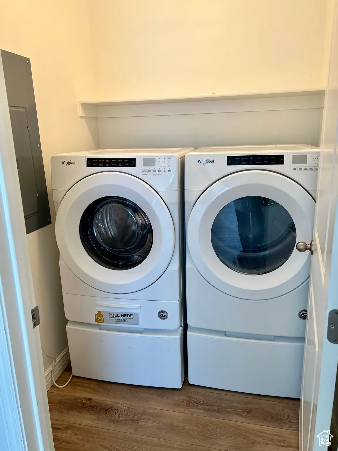Laundry room, wood finished floors, electric panel, and washing machine and clothes dryer