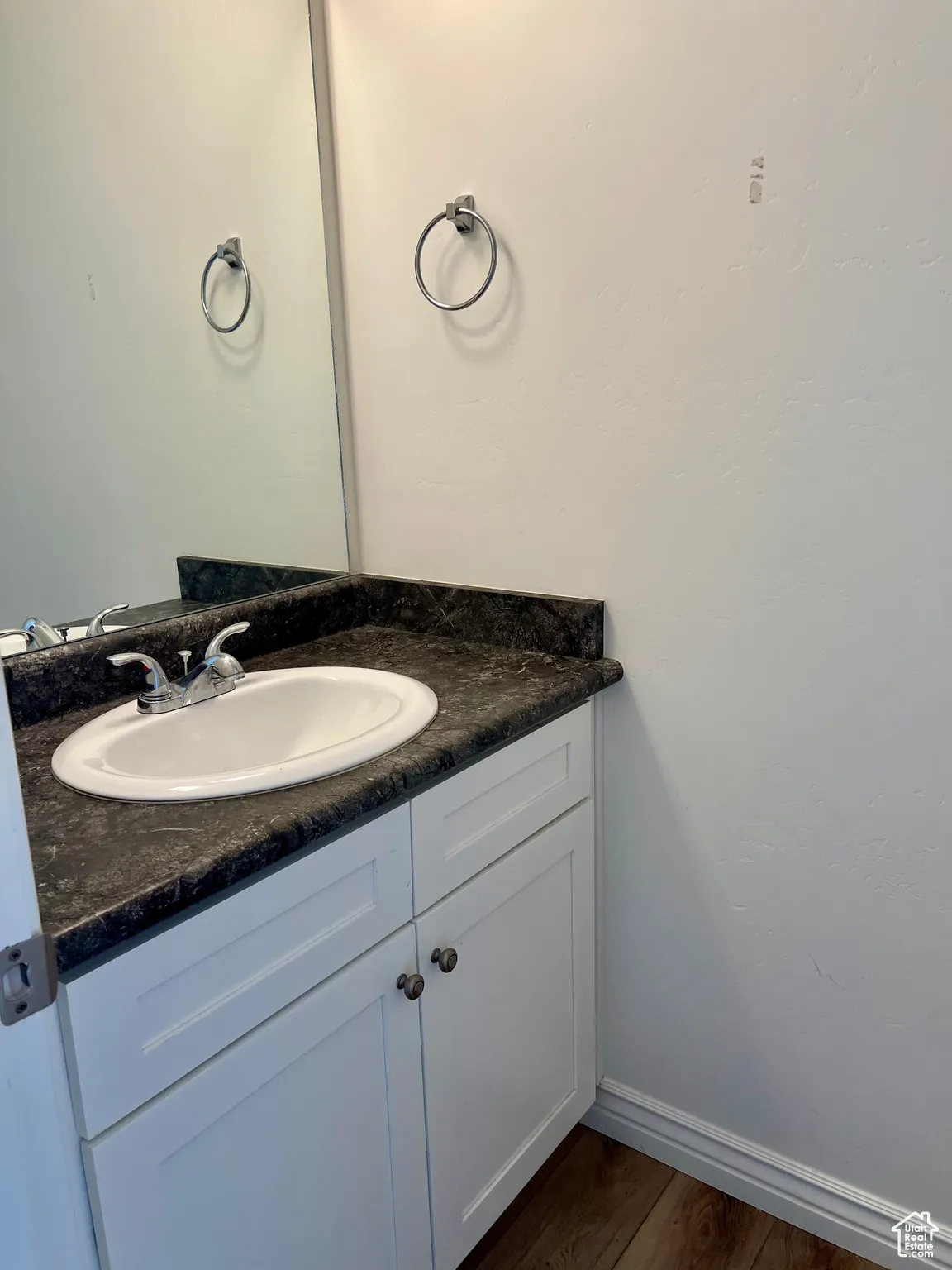 Half bath off of main floor living room. Bathroom with vanity and dark wood finished floors