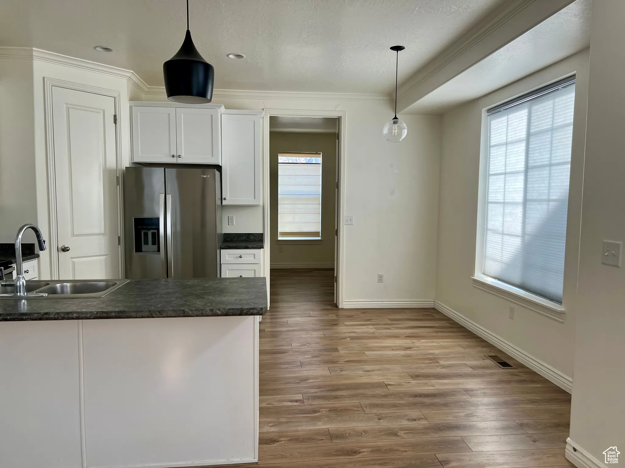 Kitchen featuring white cabinetry, stainless steel fridge, pendant lighting, light wood finished floors, and crown molding