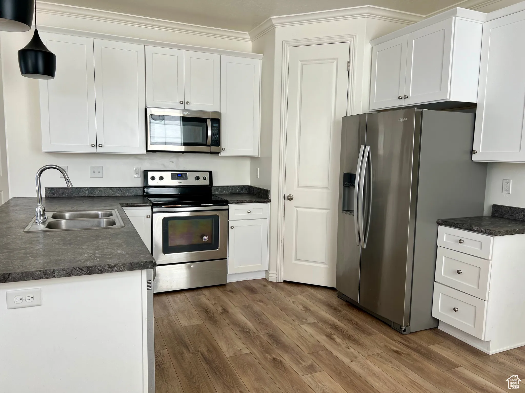 Kitchen with dark countertops, appliances with stainless steel finishes, dark wood-type flooring, white cabinets, and hanging light fixtures