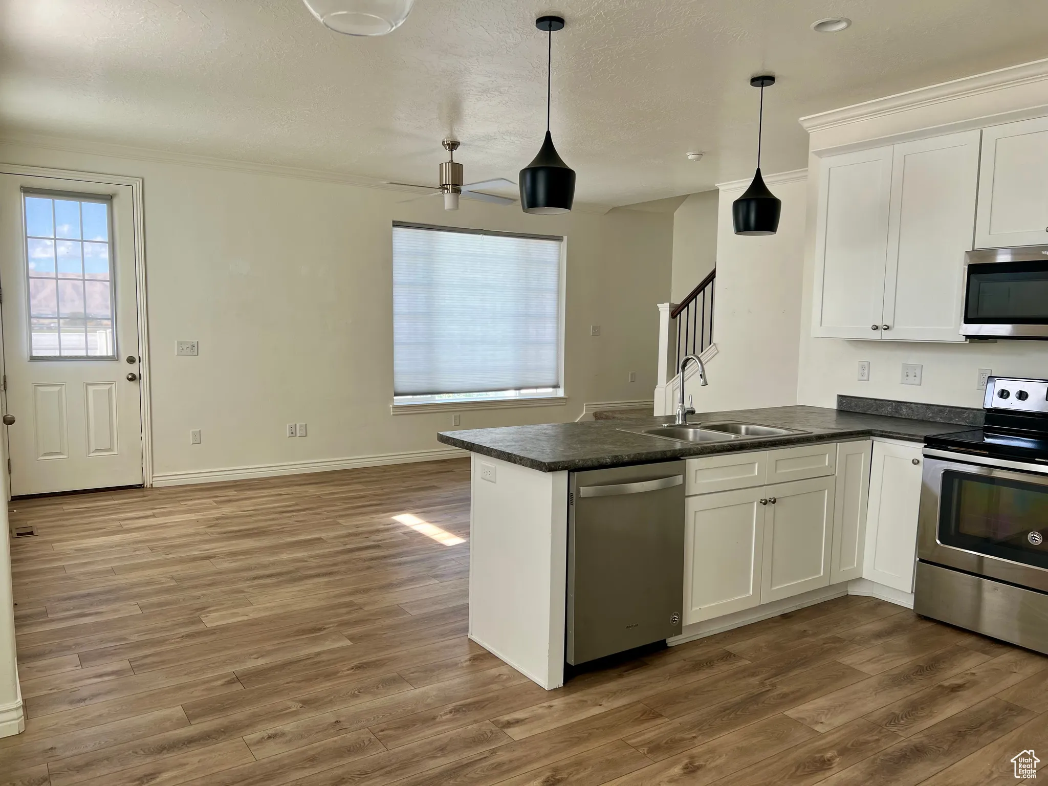Kitchen featuring appliances with stainless steel finishes, a peninsula, white cabinetry, dark wood-style flooring, and hanging light fixtures