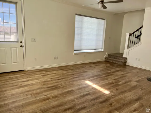 Unfurnished living room with wood finished floors, ornamental molding, stairs, and a ceiling fan