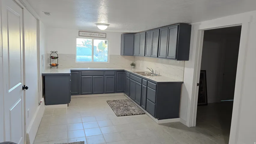 Kitchen featuring ample dark gray cabinetry, light-toned countertops, a white tile backsplash, and a stainless steel sink with a single-handle faucet