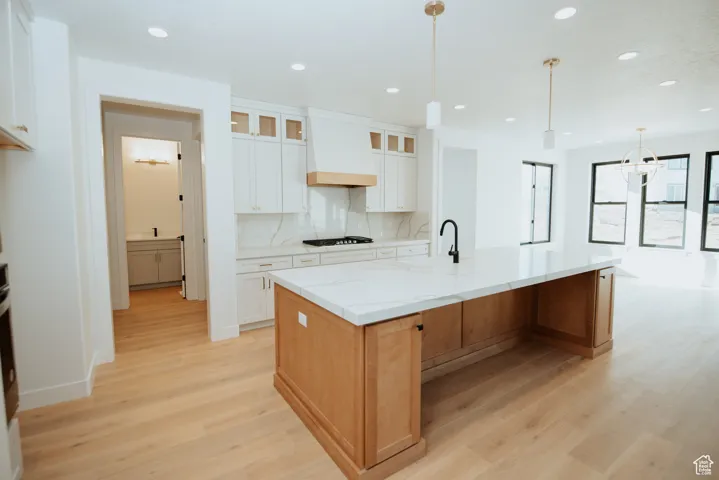 Kitchen featuring glass insert cabinets, backsplash, pendant lighting, light stone counters, and a spacious island
