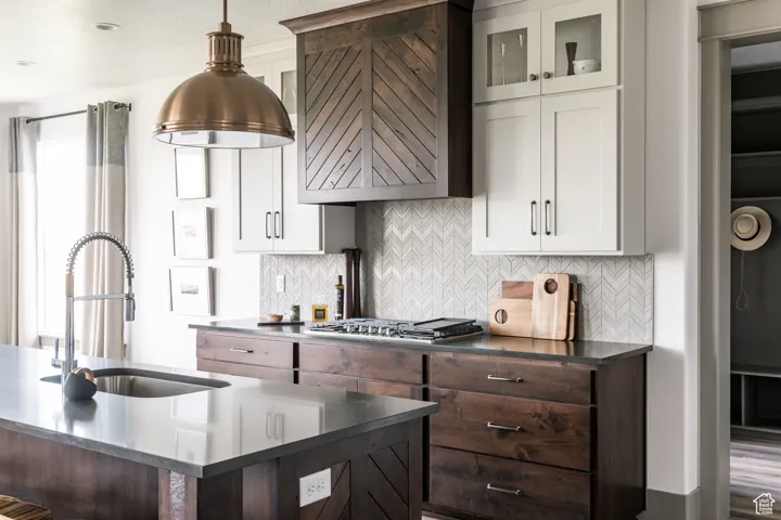 Kitchen featuring tasteful backsplash, dark brown cabinetry, white cabinetry, hanging light fixtures, and glass insert cabinets