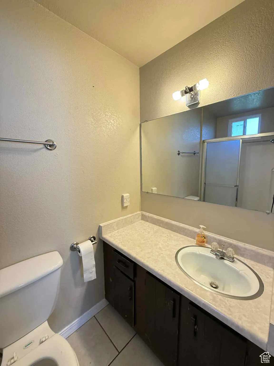 Master bathroom with a textured wall, light tile patterned flooring, a shower stall, and vanity