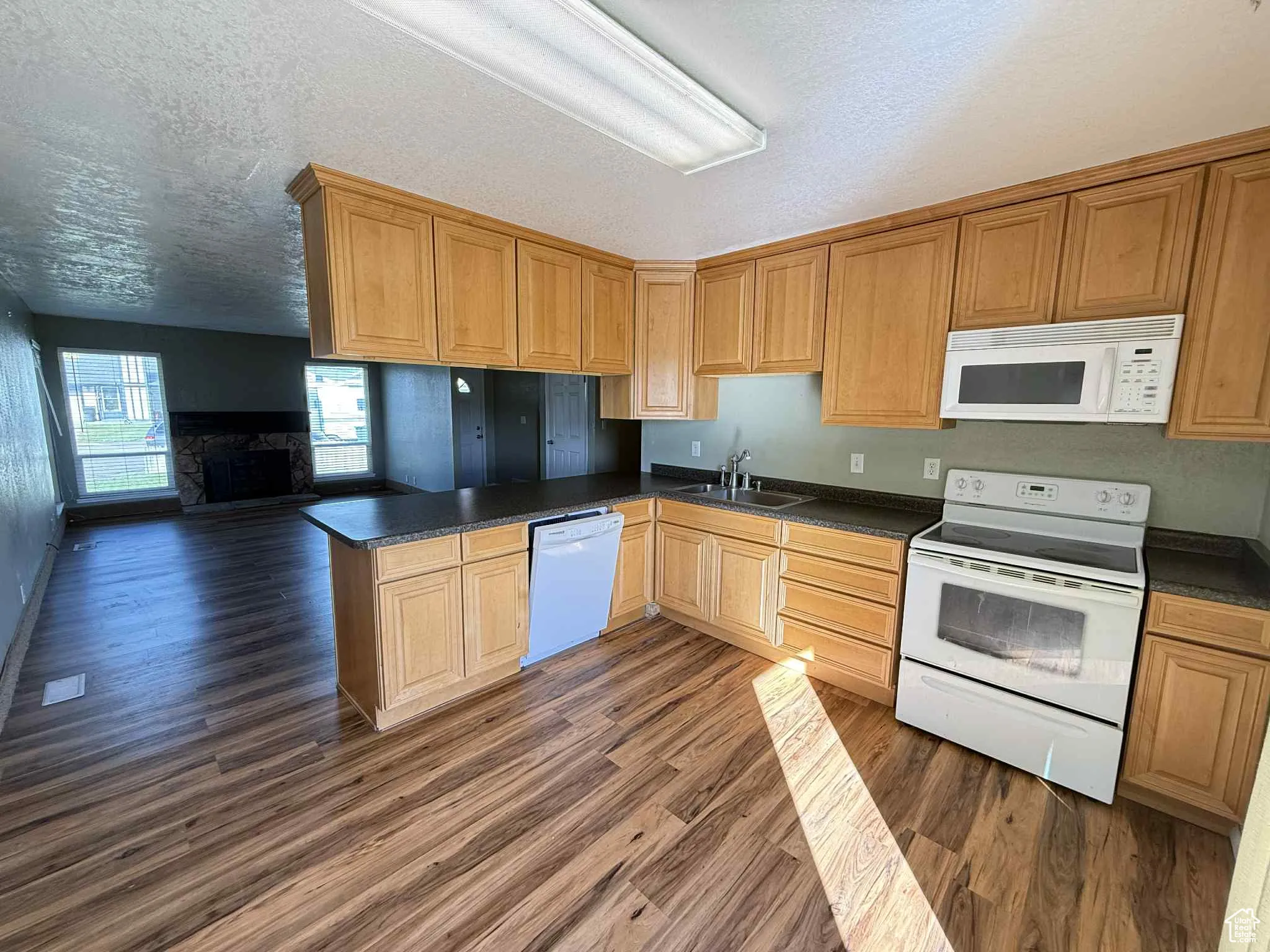 Kitchen with white appliances, dark countertops, dark wood-style flooring, a textured ceiling, and a peninsula