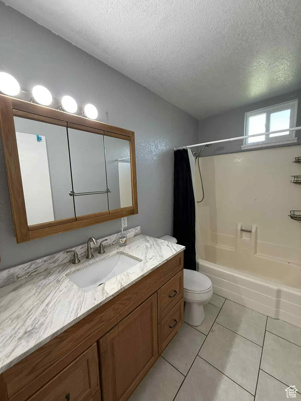Main Bathroom with shower / tub combo with curtain, a textured ceiling, light tile patterned flooring, and vanity