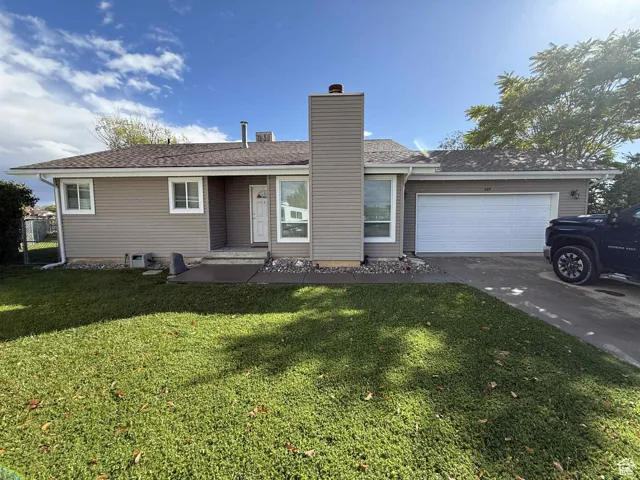 Single story home featuring driveway, a front lawn, a chimney, roof with shingles, and an attached garage