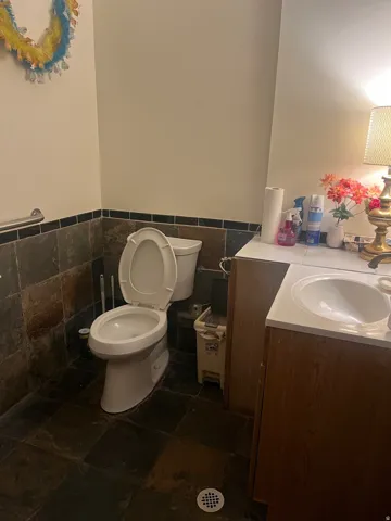 Slate tile flooring with coordinating wainscoting, white toilet, and a vanity with an integrated sink