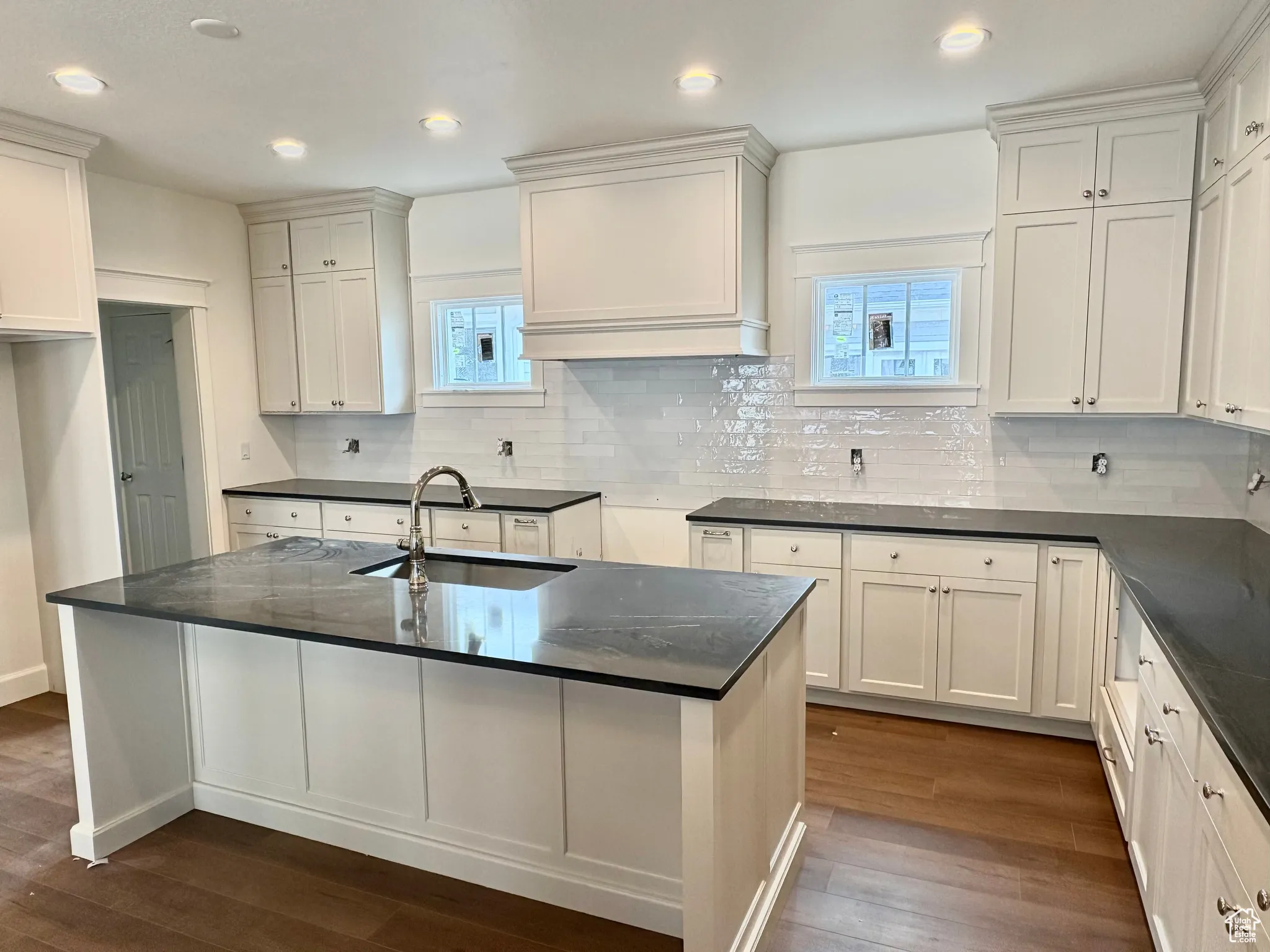 Kitchen featuring decorative backsplash, dark wood-type flooring, recessed lighting, white cabinets, and a center island with sink