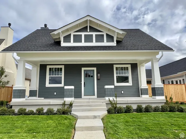 View of front of home with roof with shingles, a front lawn, and covered porch