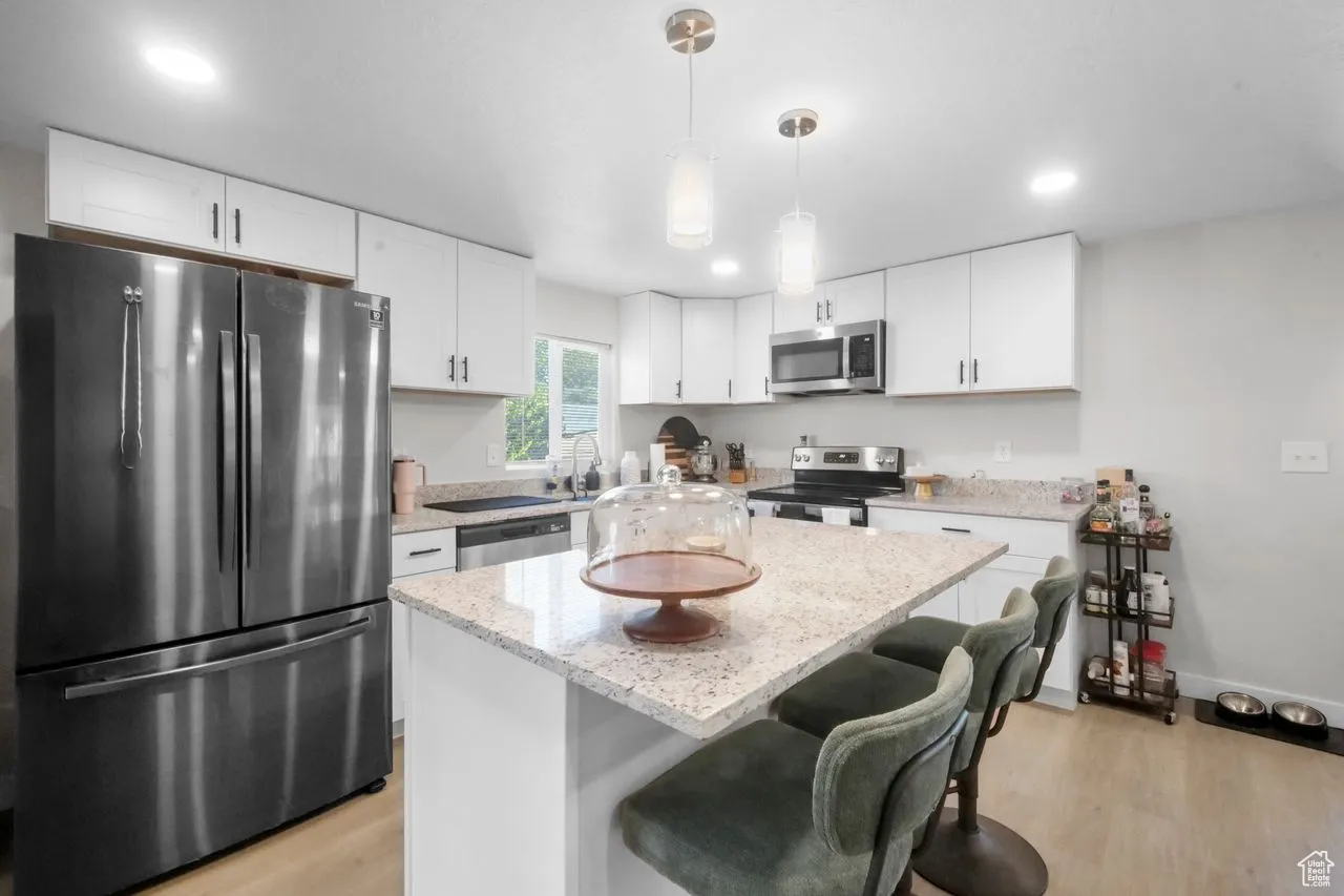 Kitchen with appliances with stainless steel finishes, light wood-style flooring, a kitchen breakfast bar, a center island, and decorative light fixtures