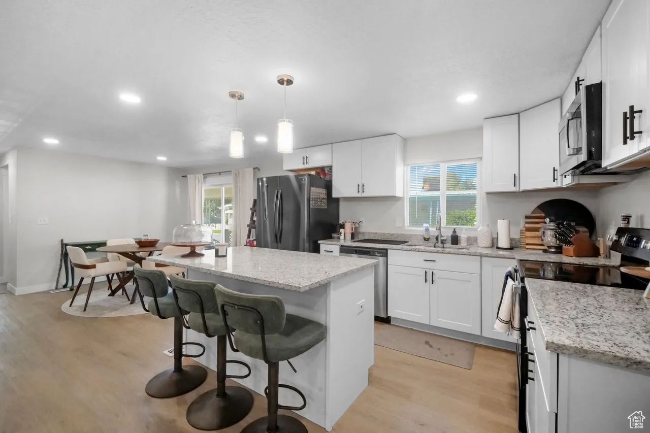 Kitchen with appliances with stainless steel finishes, a kitchen breakfast bar, a kitchen island, light stone countertops, and light wood-style flooring