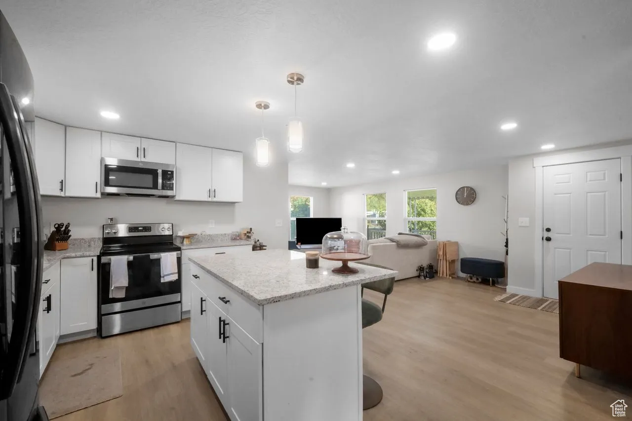Kitchen featuring stainless steel appliances, open floor plan, a kitchen island, light wood-style flooring, and white cabinets