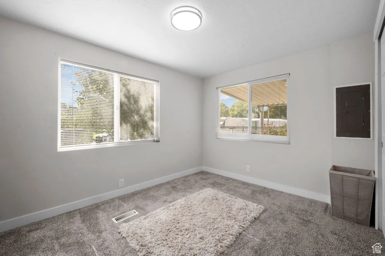 Carpeted empty room with electric panel and baseboards