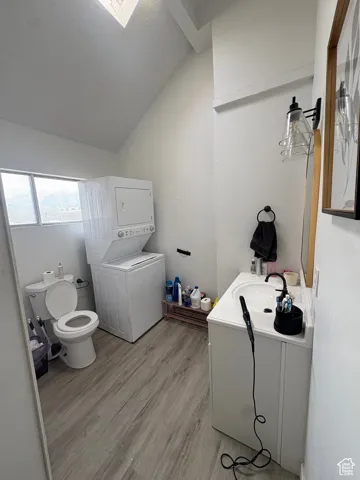 3/4 bath with vanity, light wood-type flooring, stacked washing machine and dryer, and lofted ceiling