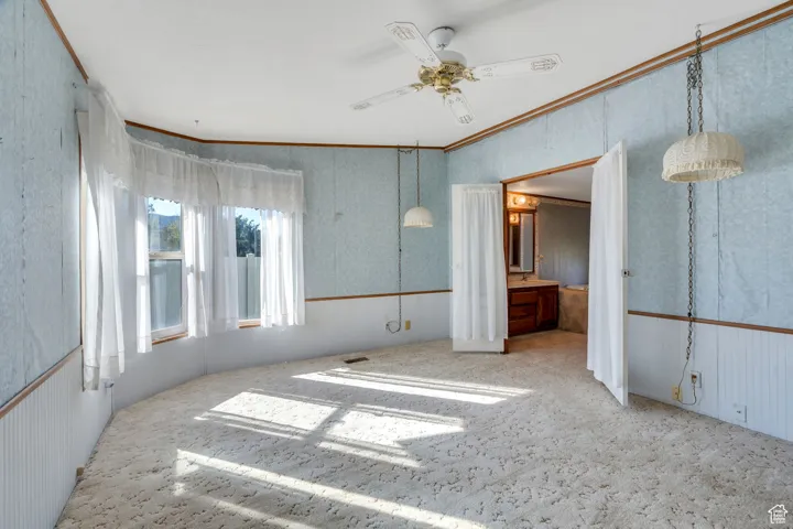 Unfurnished bedroom with ornamental molding, a ceiling fan, carpet floors, wallpapered walls, and a wainscoted wall