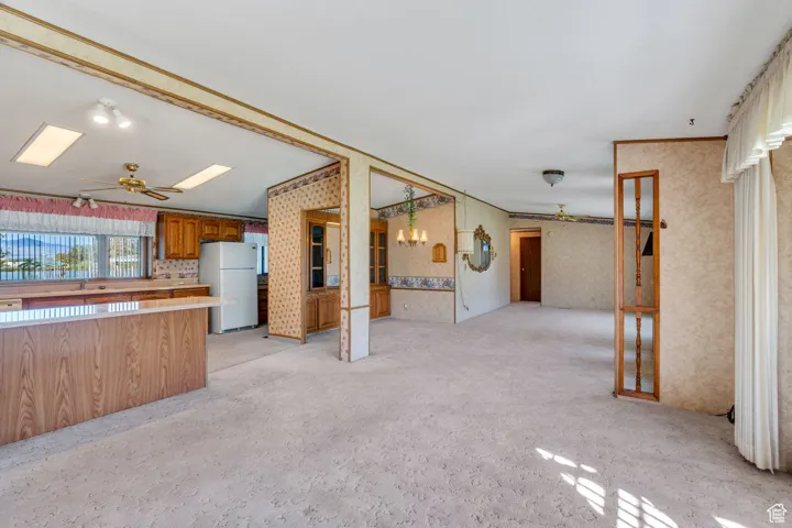 Kitchen with ceiling fan, light countertops, brown cabinetry, freestanding refrigerator, and open floor plan