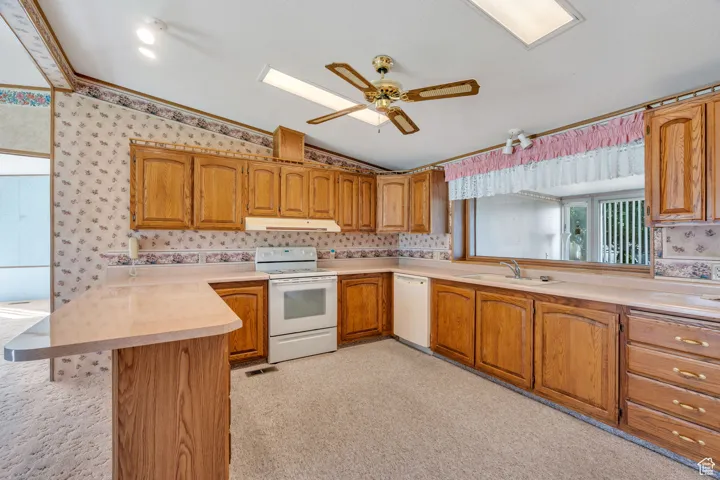Kitchen with lofted ceiling, a peninsula, white appliances, light countertops, and brown cabinetry
