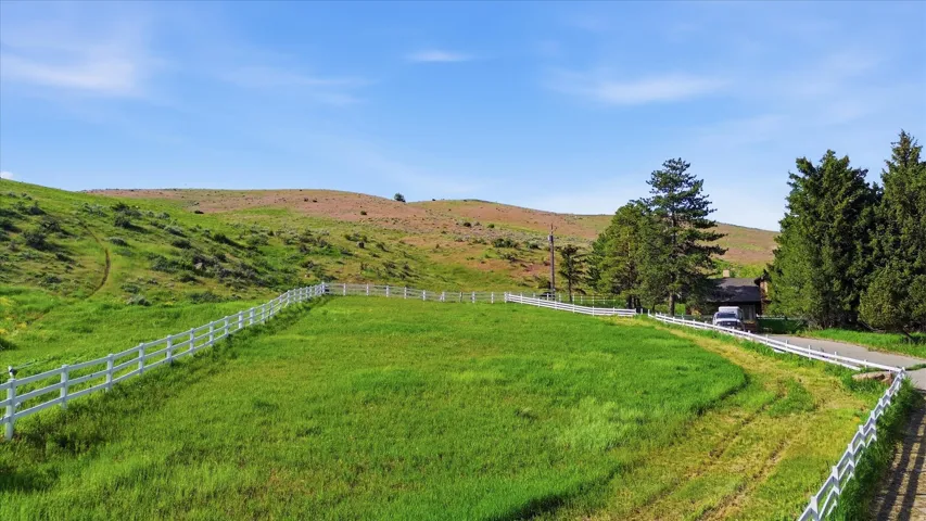 Expansive fenced pasture with lush green grass and rolling hills in the background