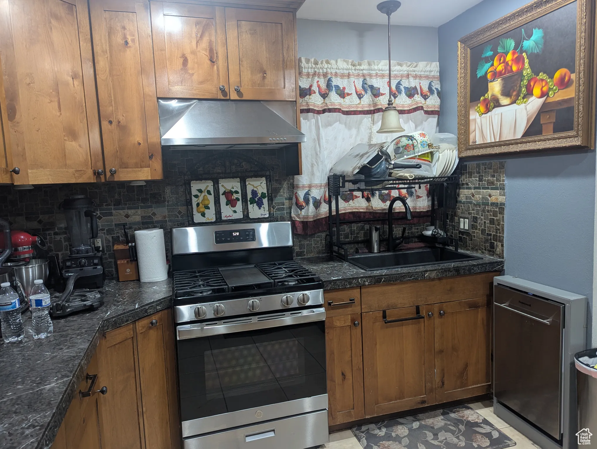 Kitchen with tasteful backsplash, appliances with stainless steel finishes, exhaust hood, and brown cabinetry