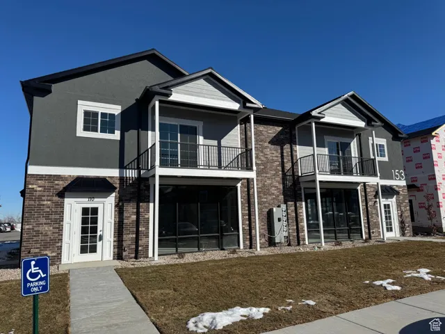 Traditional-style home with a balcony, brick siding, stucco siding, and a front yard