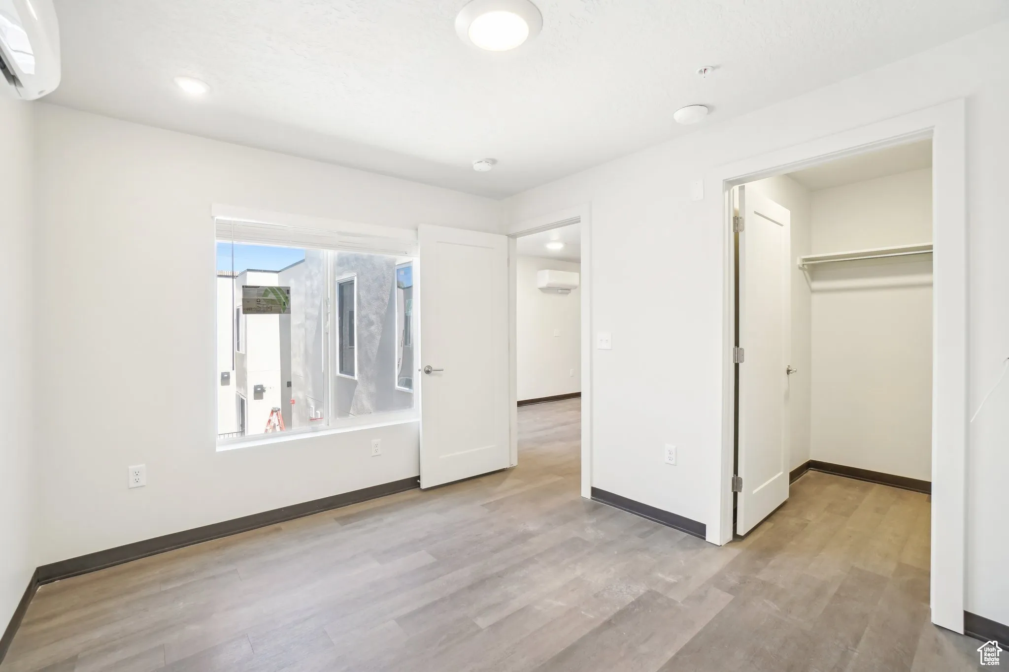 Unfurnished bedroom featuring light wood-style floors, a walk in closet, and a wall mounted air conditioner