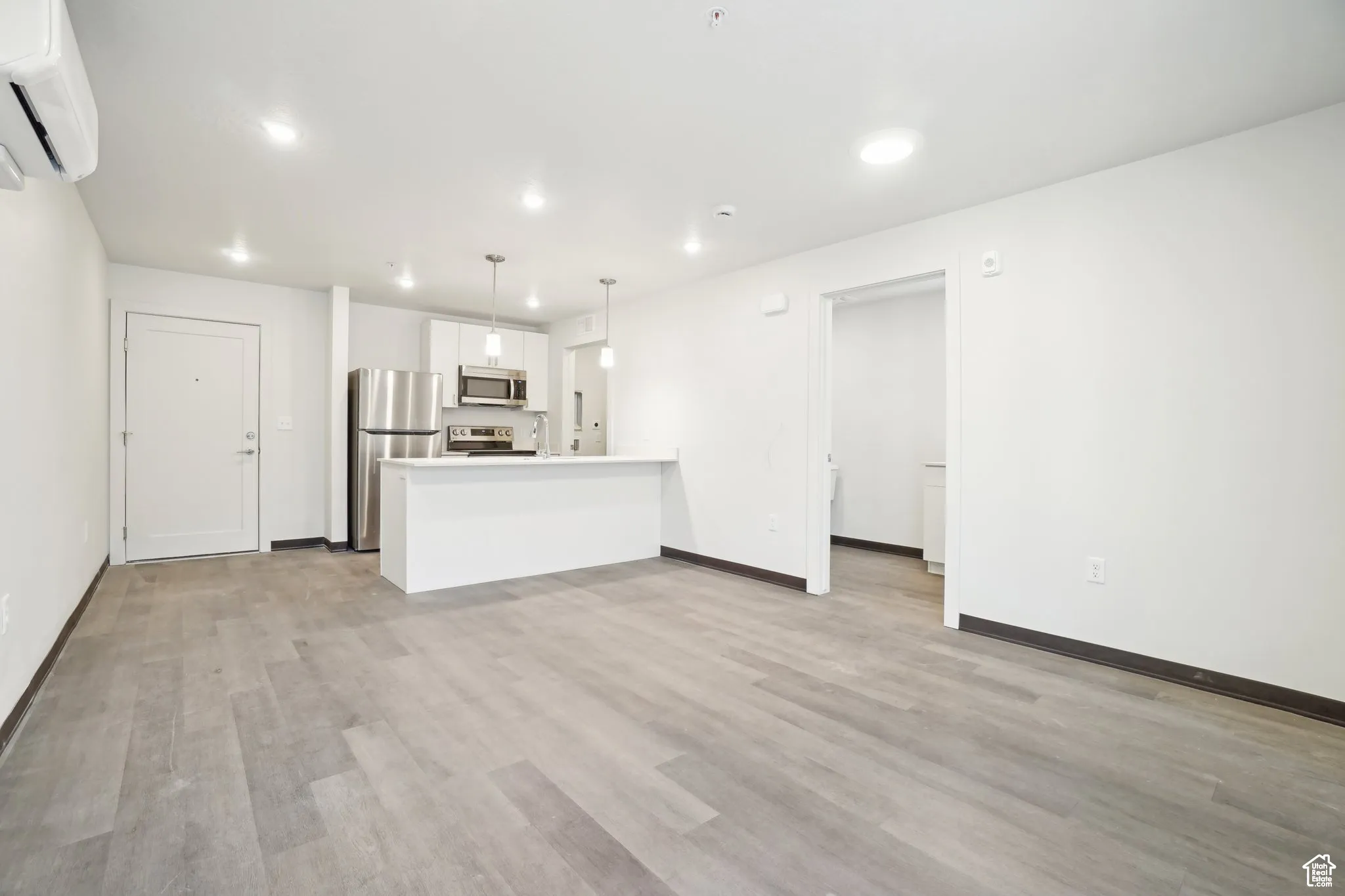 Unfurnished living room featuring a wall mounted AC, light wood-type flooring, and recessed lighting