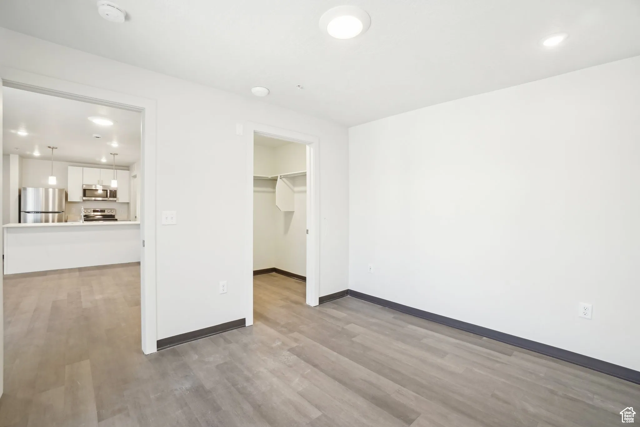 Unfurnished bedroom featuring recessed lighting, freestanding refrigerator, a walk in closet, and light wood-style floors