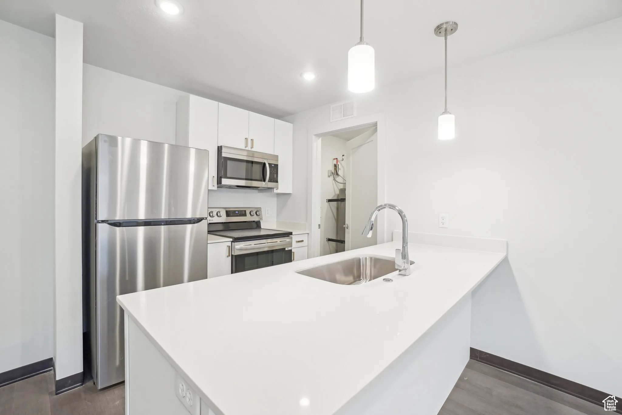 Kitchen featuring appliances with stainless steel finishes, a peninsula, white cabinetry, hanging light fixtures, and recessed lighting