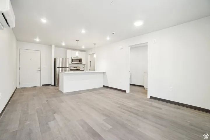 Unfurnished living room featuring a wall mounted AC, light wood-type flooring, and recessed lighting