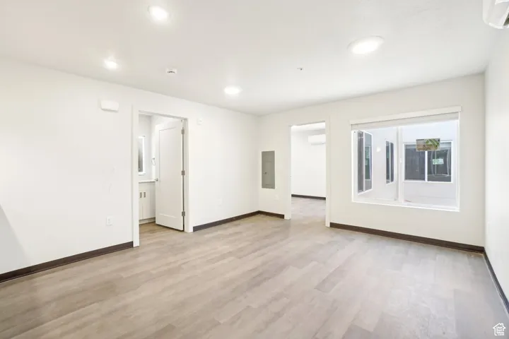 Spare room with light wood-type flooring, recessed lighting, electric panel, a wall unit AC, and an AC wall unit