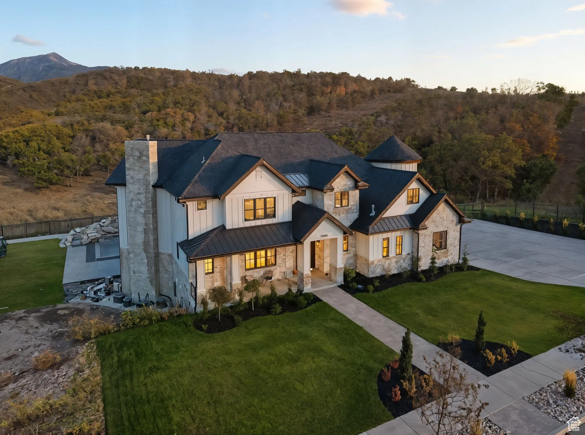 Modern inspired farmhouse featuring a standing seam roof, a metal roof, stone siding, a forest view, and driveway