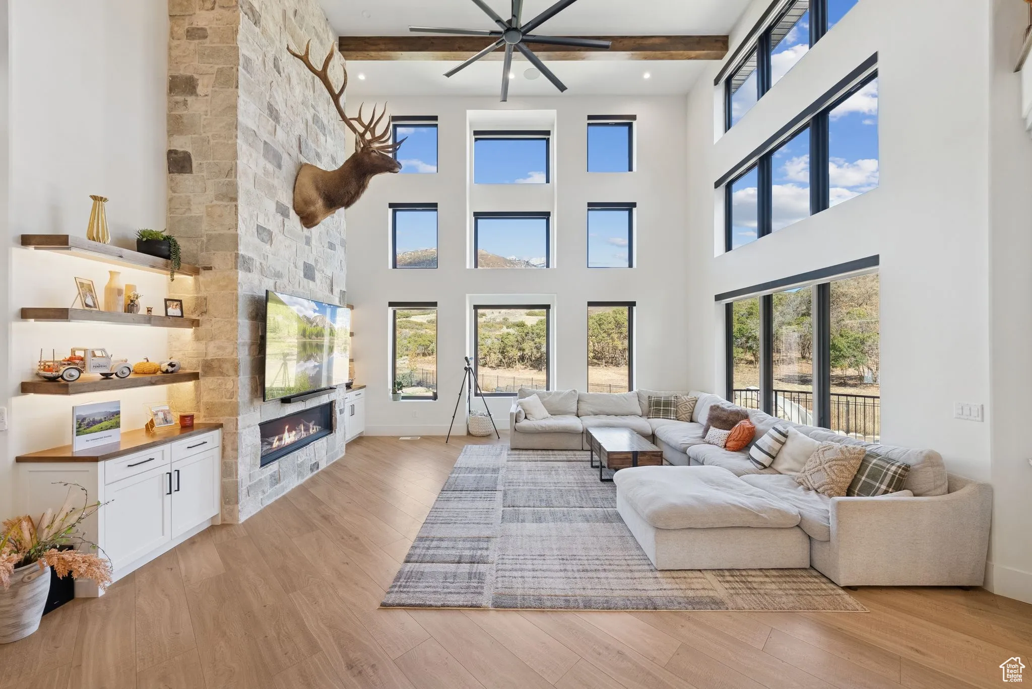Living area featuring light wood finished floors, a large fireplace, beam ceiling, and ceiling fan