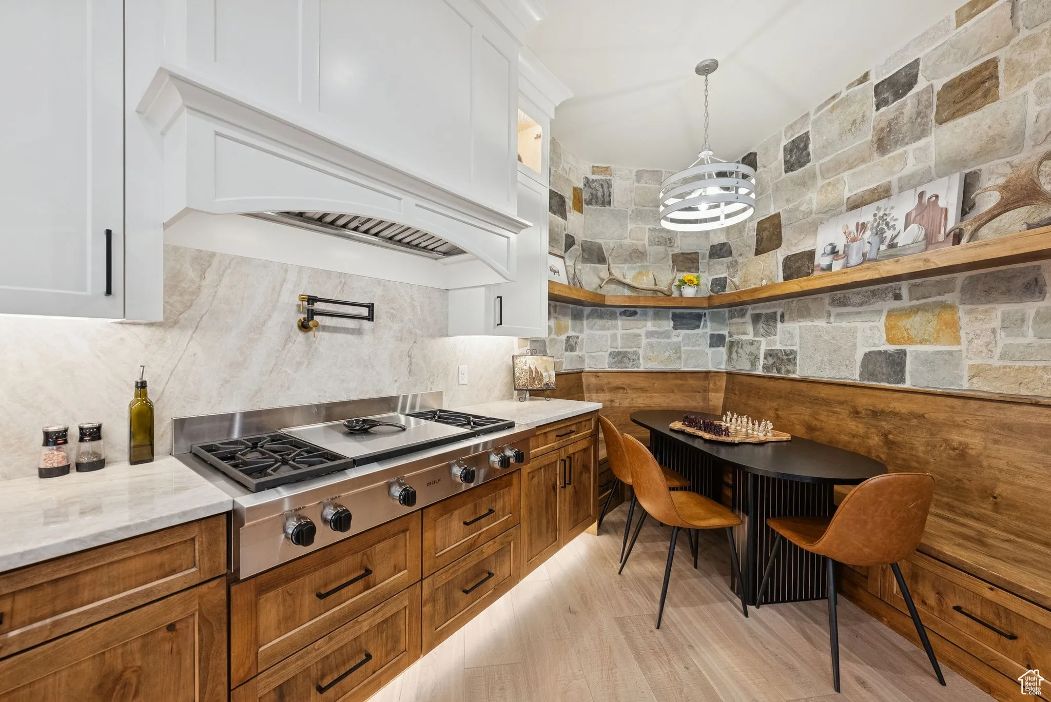 Kitchen featuring decorative light fixtures, stainless steel gas cooktop, light stone countertops, glass insert cabinets, and white cabinets