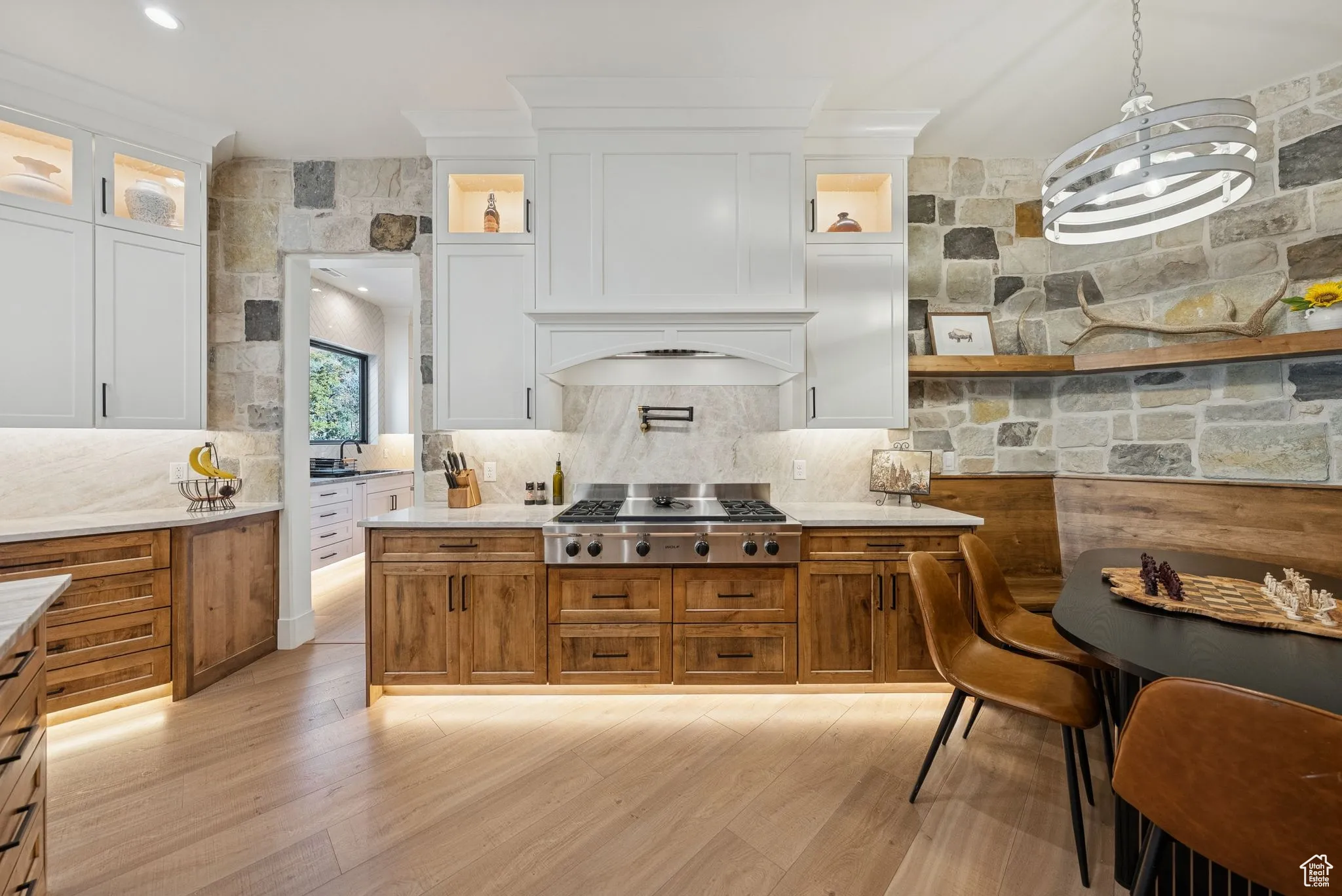 Kitchen featuring brown cabinetry, hanging light fixtures, light stone counters, and decorative backsplash