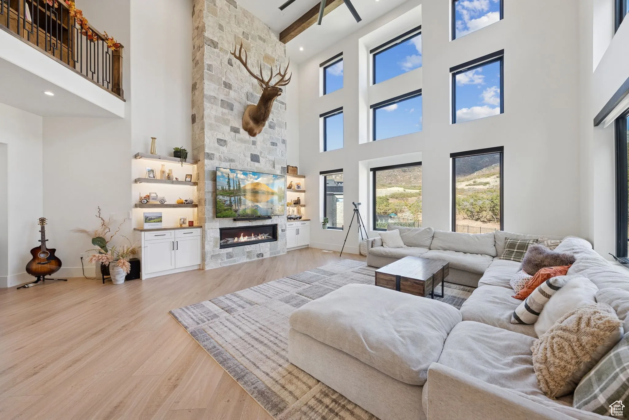 Living room with light wood-type flooring, a stone fireplace, a high ceiling, a ceiling fan, and recessed lighting