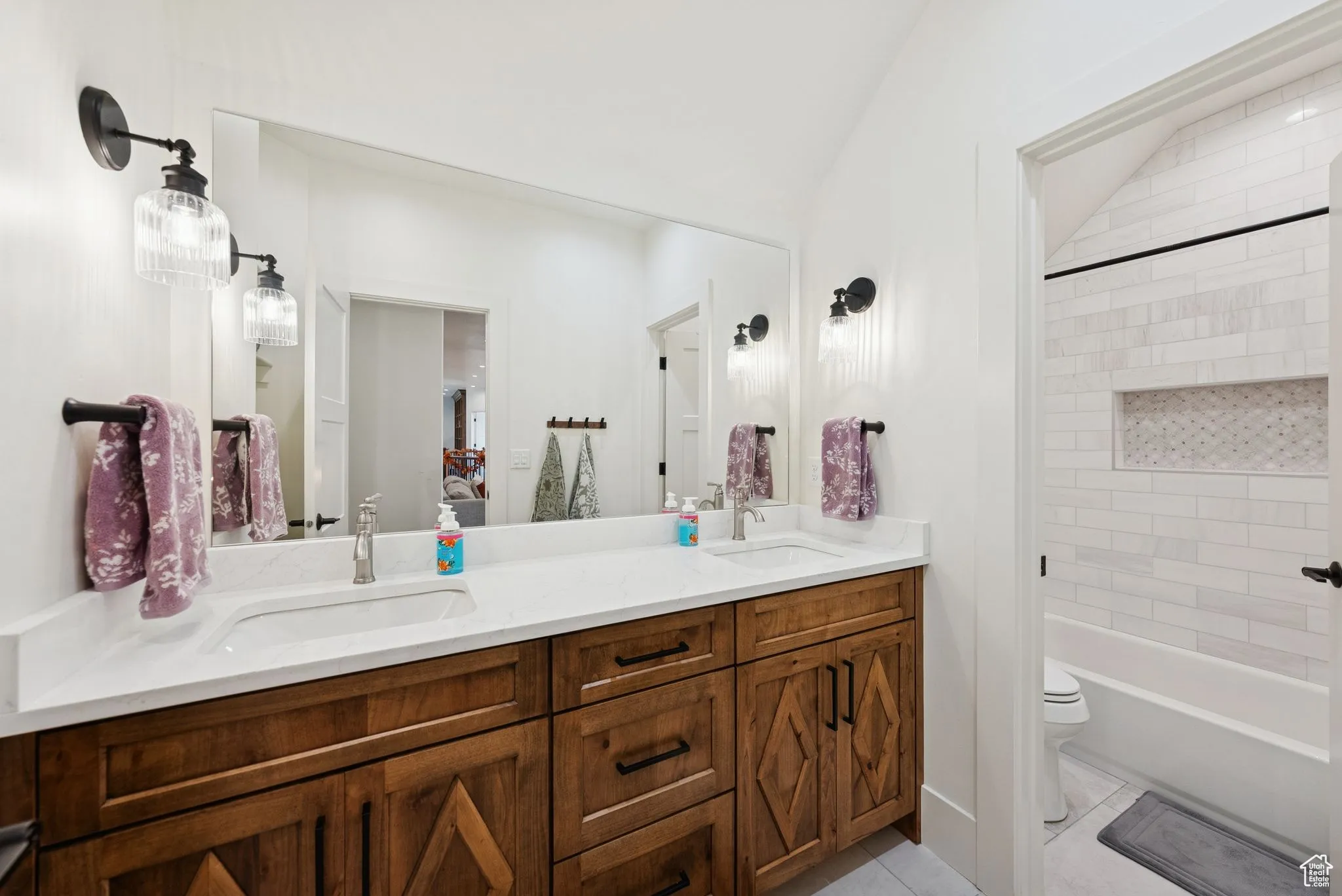 Bathroom with double vanity, light tile patterned floors, and shower / washtub combination
